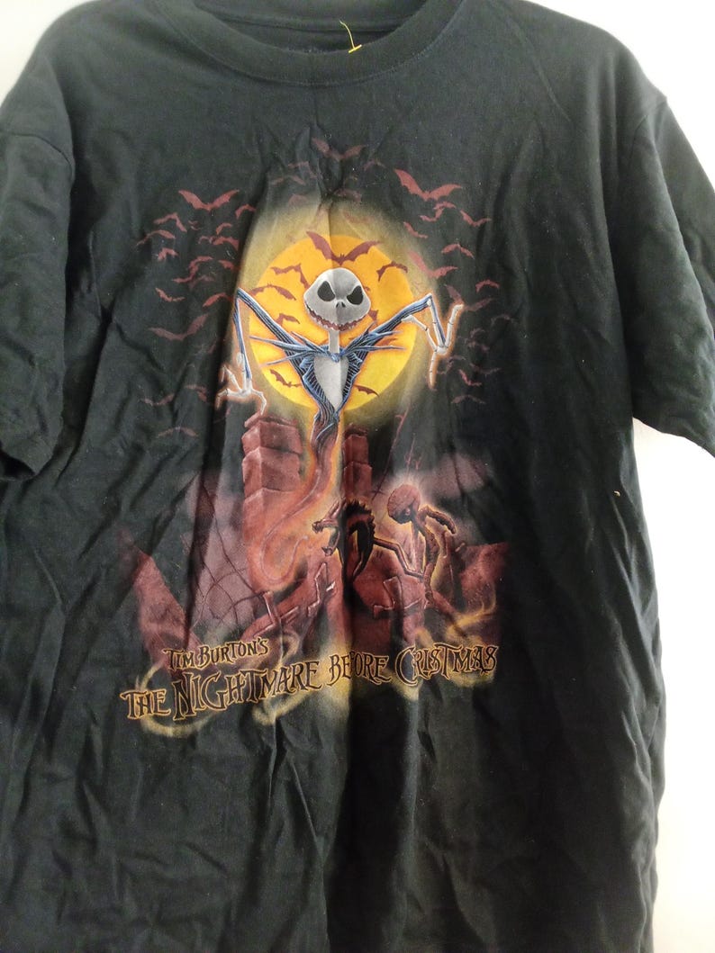 May include: Black t-shirt featuring a graphic from Tim Burton's "The Nightmare Before Christmas." The design includes Jack Skellington in front of a full moon, bats, and the film's title. The shirt is a short-sleeved crew neck.
