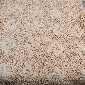 May include: Cream-colored, crocheted tablecloth with a repeating spiral pattern. The intricate openwork design creates a delicate, textured surface. The edges of the tablecloth are scalloped.