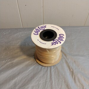 May include: A spool of white Craft Lace Toner Plaited string. The spool is white with purple lettering and a black center.