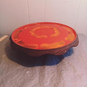May include: A round ceramic serving tray with a wavy edge. The tray is red with a concentric circle design in a lighter orange color.