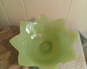 May include: A light green glass bowl with a star-shaped rim. The bowl has a smooth, glossy finish and a shallow, rounded interior. The bowl is sitting on a white surface.