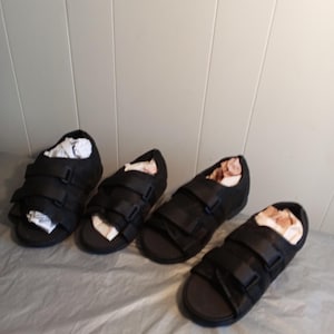 Puede incluir: Cuatro sandalias ortopédicas negras con correas ajustables. Las sandalias tienen cierre de velcro y están diseñadas para la comodidad y el apoyo.