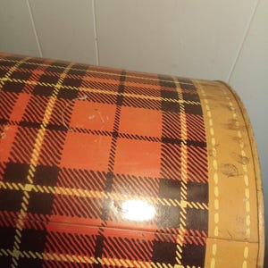 May include: A vintage metal container with a red, black, and yellow plaid pattern. The container has a rounded shape and a tan border with a dotted design. The plaid design is a classic pattern.