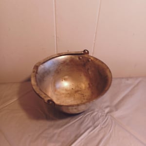 May include: A silver metal bowl with a rounded bottom and two handles. The bowl is slightly dented and has a worn surface.