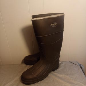 May include: A pair of brown rubber boots. The boots are tall, reaching the mid-calf, with a ridged sole and a reinforced toe. The brand name "SERVUS" is visible on the upper shaft. The boots are designed for outdoor use and protection.