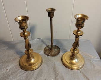 Può includere: Tre portacandele in ottone. Due dei portacandele hanno un design decorativo e una base rotonda. Il terzo portacandele è un design semplice e alto con una base rotonda.