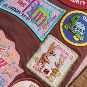 May include: A collection of embroidered patches in various shapes and colors. One patch reads "Join the Fun!" with "GS Cookies '06-'07" below. Another features two brown bunnies with the text "Mom & Me". Other patches include a turtle and stars.