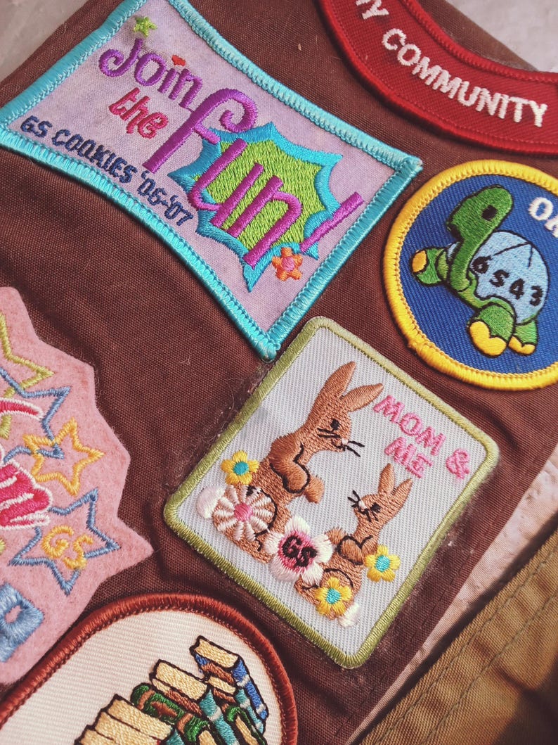 May include: A collection of embroidered patches in various shapes and colors. One patch reads "Join the Fun!" with "GS Cookies '06-'07" below. Another features two brown bunnies with the text "Mom & Me". Other patches include a turtle and stars.