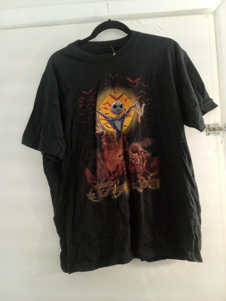 May include: Black t-shirt featuring a graphic from "The Nightmare Before Christmas." The design includes Jack Skellington in front of a full moon, bats, and the text "The Nightmare Before Christmas."