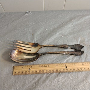 May include: A silver salad serving set with a fork and spoon. The set is on a white surface with a ruler for scale.