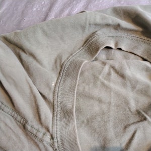 Puede incluir: Primer plano del cuello de una camiseta verde. La tela es suave y tiene una apariencia ligeramente texturizada.