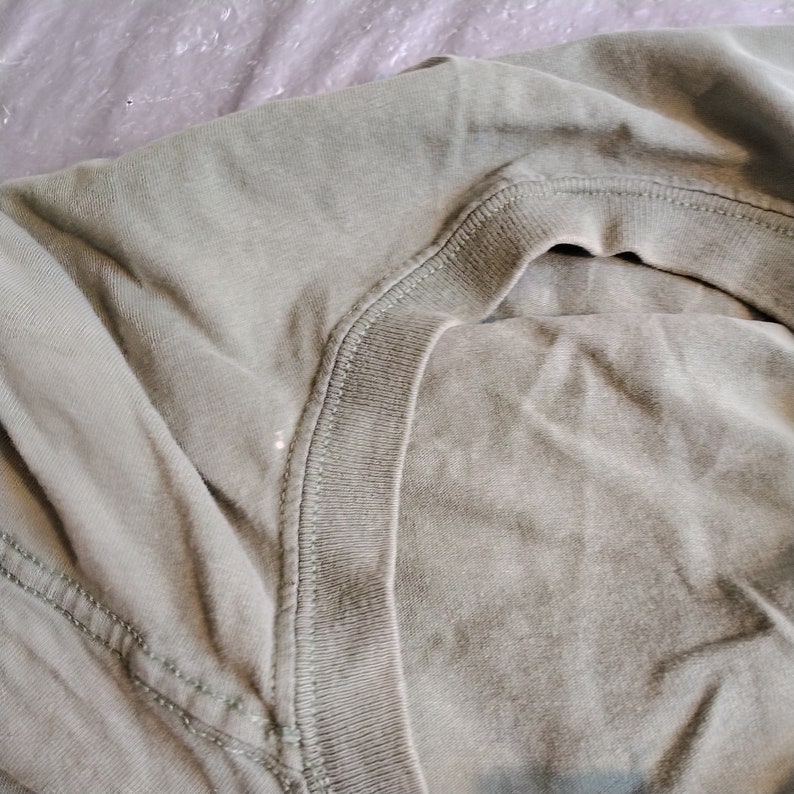 Puede incluir: Primer plano del cuello de una camiseta verde. La tela es suave y tiene una apariencia ligeramente texturizada.