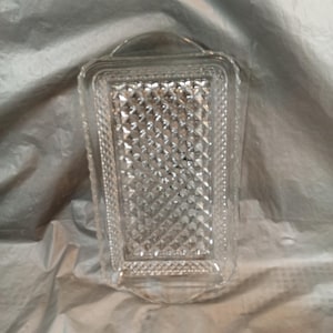 May include: Clear glass rectangular dish with a diamond pattern in the center and a handle on top. The dish has a decorative border and is likely used for serving or display.