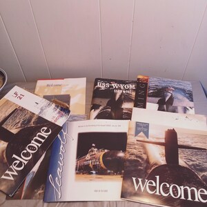 May include: A collection of six welcome brochures for a submarine, featuring images of the submarine and the text "Welcome aboard".