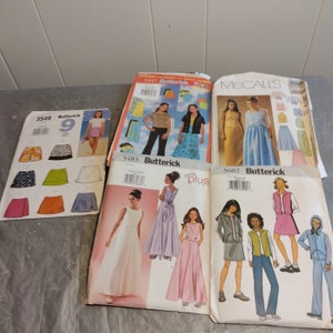 May include: A collection of sewing patterns for girls' clothing. The patterns are from the brands McCall's and Butterick. The patterns include designs for skirts, dresses, shorts, and tops. The patterns are in various colors, including pink, blue, green, and white.