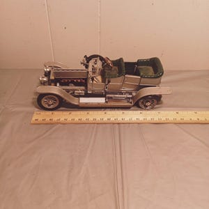 Puede incluir: Un coche modelo plateado con un interior verde y un motor detallado. El coche está sobre una superficie marrón con una regla de madera.