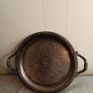 May include: A silver-toned metal serving tray with two handles. The tray has an ornate, embossed design on the surface and a braided edge. The text "RECC A FLT WINNER 1981" is engraved in the center.