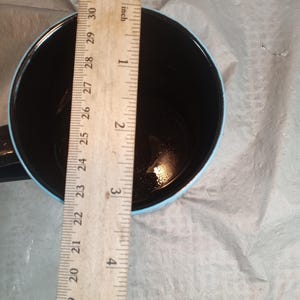 Pu&ograve; includere: Una tazza da caff&egrave; nera con bordo e manico azzurro. Un righello di legno &egrave; posto all'interno della tazza, mostrando una profondit&agrave; di circa 7,6 cm.