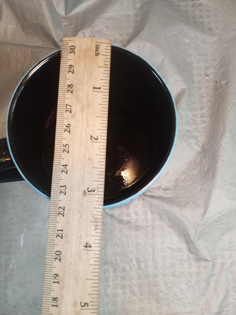 Pu&ograve; includere: Una tazza da caff&egrave; nera con bordo e manico azzurro. Un righello di legno &egrave; posto all'interno della tazza, mostrando una profondit&agrave; di circa 7,6 cm.