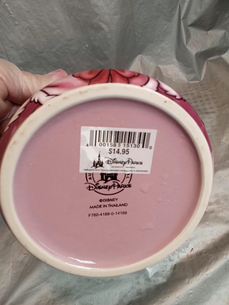 Puede incluir: Un cuenco rosa de cer&aacute;mica de Disney Parks con borde blanco y dise&ntilde;o floral. La parte inferior del cuenco tiene un interior rosa y una pegatina de Disney Parks. Hecho en Tailandia.