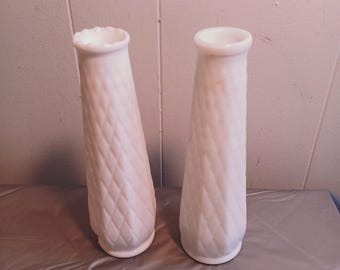 May include: Two white milk glass vases with a diamond pattern. The vases are tall and slender.