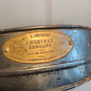 Könnte beinhalten: Ein vintage, ovalförmiges, messingfarbenes Metallschild mit dem Text "S. Bowers' Trade Mark American Broiler Pat. July 21, 1868. Oct. 19, 1869. American Broiler Co. Prop'rs."