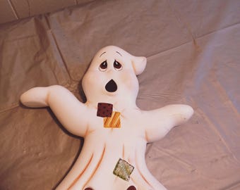 Può includere: Una statuetta di fantasma in ceramica bianca con un'espressione sorpresa. Il fantasma ha toppe di stoffa marrone, gialla e verde sul corpo.