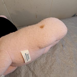 May include: A plush toy in shades of pink and black, with a small tag that reads "Disneyland Walt Disney World &copy;1994 Disney". The toy has a brown stain on its surface.