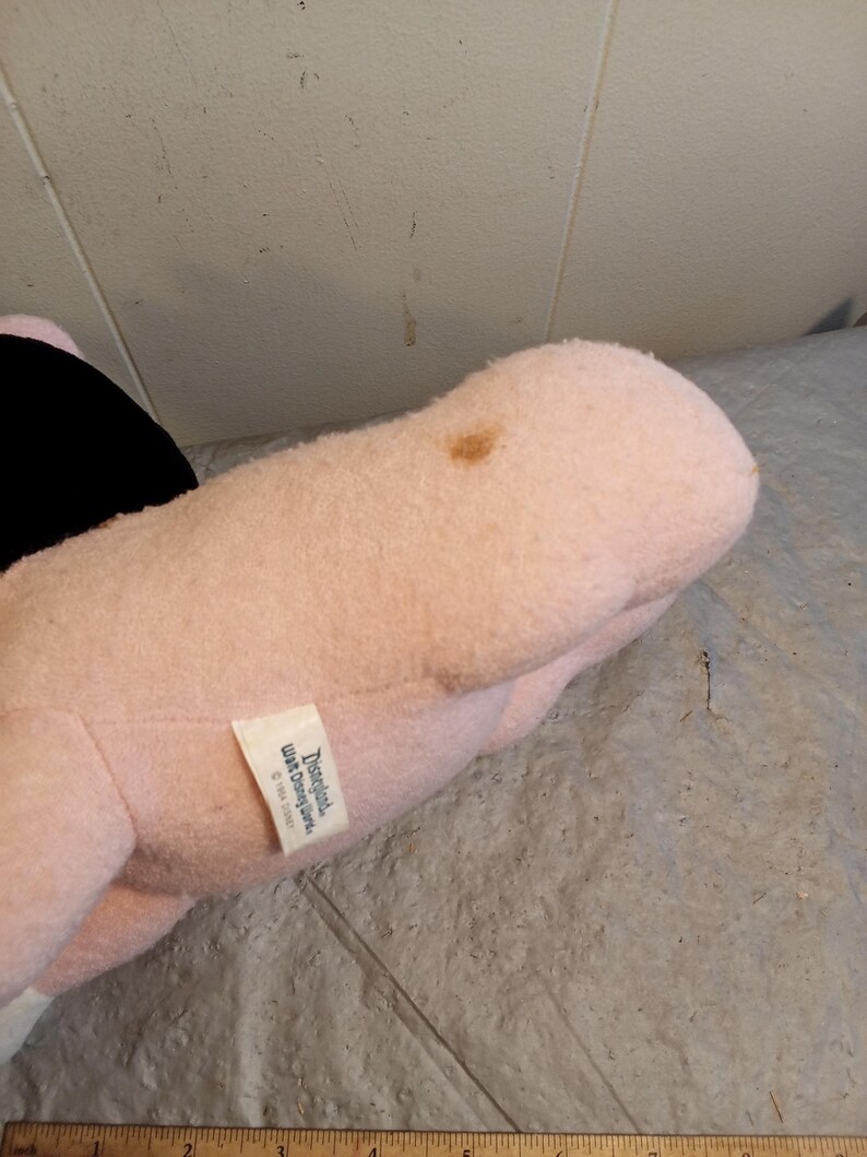 May include: A plush toy in shades of pink and black, with a small tag that reads "Disneyland Walt Disney World &copy;1994 Disney". The toy has a brown stain on its surface.