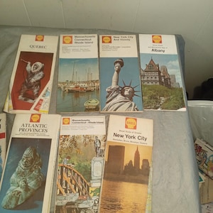 Può includere: Una collezione di mappe turistiche Shell vintage. Le mappe presentano illustrazioni di varie località, tra cui Quebec, New York City e Albany. Le mappe sono di varie dimensioni e colori, con il logo Shell in evidenza.