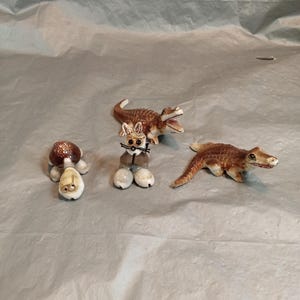 May include: A collection of ceramic animal figurines, including a tortoise, a rabbit, and two alligators. The tortoise has a brown shell and a cream-coloured body. The rabbit has a brown body and white legs. The alligators are brown.