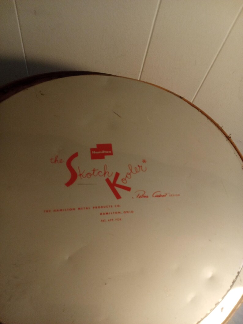 May include: Vintage "Skotch Kooler" metal cooler lid. The lid is off-white with red lettering and a red square logo. The text includes "the Skotch Kooler" and "The Hamilton Metal Products Co., Hamilton, Ohio."