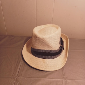 May include: A white straw hat with a black ribbon band. The hat has a wide brim and a slightly indented crown.