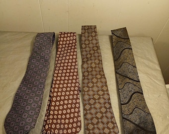 May include: Four patterned neckties in shades of purple, brown, and gold are displayed. The ties feature various geometric and floral designs. The ties are laid out on a light-colored surface, showcasing their different patterns and colors.