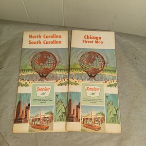 Può includere: Due mappe turistiche vintage. Una è etichettata "North Carolina South Carolina" e l'altra "Chicago Street Map". Entrambe presentano una grafica del globo e il marchio Sinclair. Le mappe includono anche illustrazioni di monumenti e un'auto d'epoca.