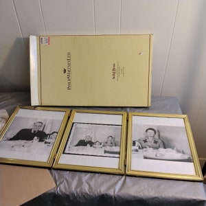 May include: Three gold-toned picture frames with black and white photographs of people. The frames are hinged together and have a box on top that says "Phillip Whitney Ltd. Solid Brass."