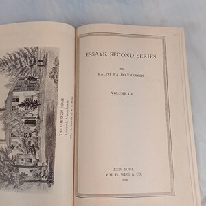 May include: An open book with the title "ESSAYS, SECOND SERIES" by Ralph Waldo Emerson. The book is Volume III, published in New York by WM. H. Wise & Co. in 1926. The left page features a black and white illustration of a house.