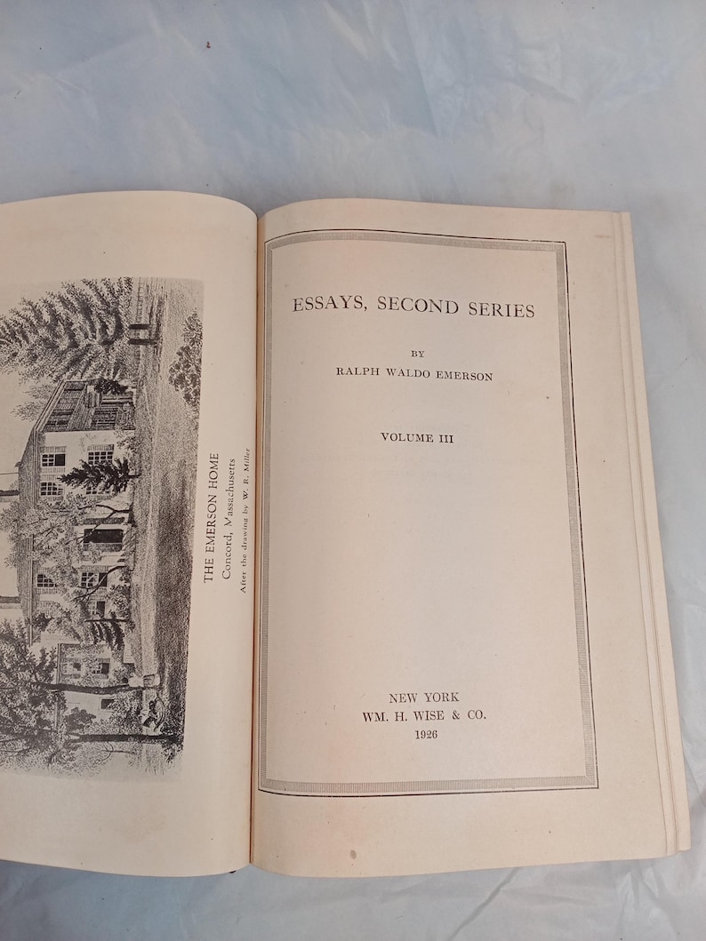 May include: An open book with the title "ESSAYS, SECOND SERIES" by Ralph Waldo Emerson. The book is Volume III, published in New York by WM. H. Wise & Co. in 1926. The left page features a black and white illustration of a house.