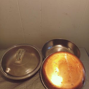 Op de afbeelding: Een set van drie zilveren potten met deksels. De potten hebben een koperen bodem en zijn op een grijs oppervlak gerangschikt.