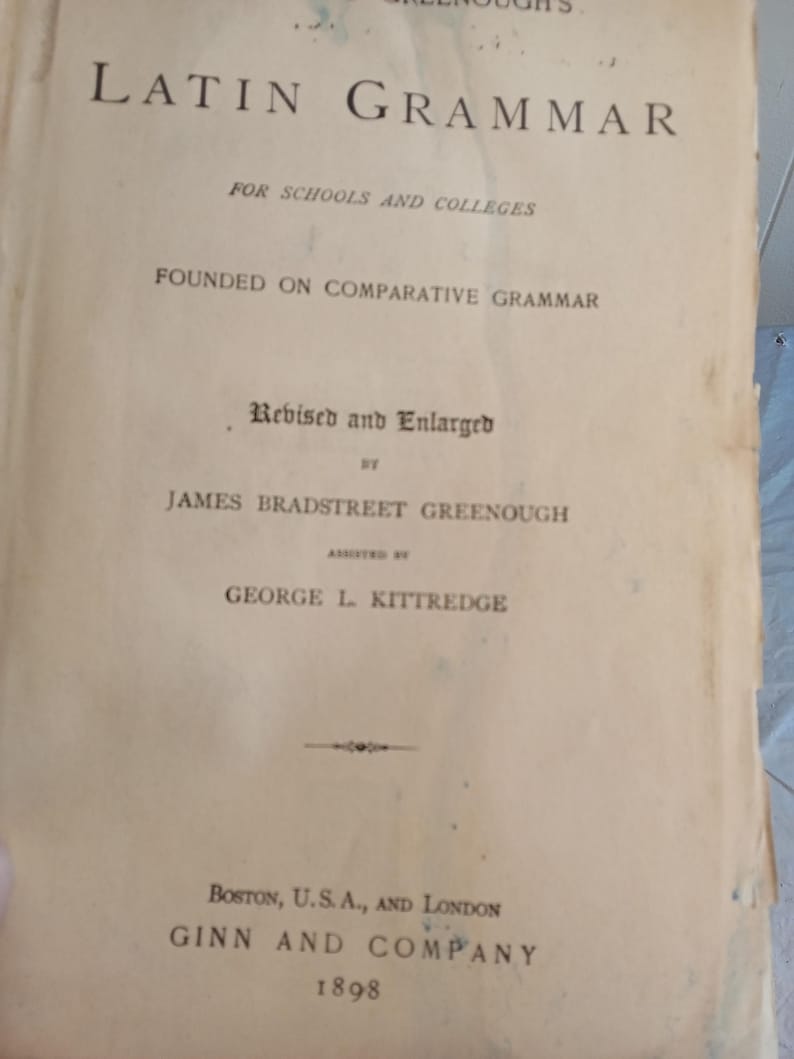 May include: An antique book titled "Latin Grammar" with text in black font. The cover is aged with visible wear and tear. The book is "Revised and Enlarged" by James Bradstreet Greenough, assisted by George L. Kittredge. Published in Boston, U.S.A., and London in 1898.