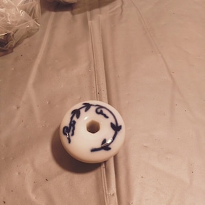 Może przedstawiać: Biały ceramiczny gałka z niebieskim wzorem kwiatowym. Gałka ma otwór w środku.