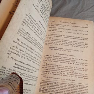 May include: Open book pages with text in Latin. The pages are aged and worn, with visible creases and a torn edge. The text is in black ink on yellowed paper, with headings and numbered sections.
