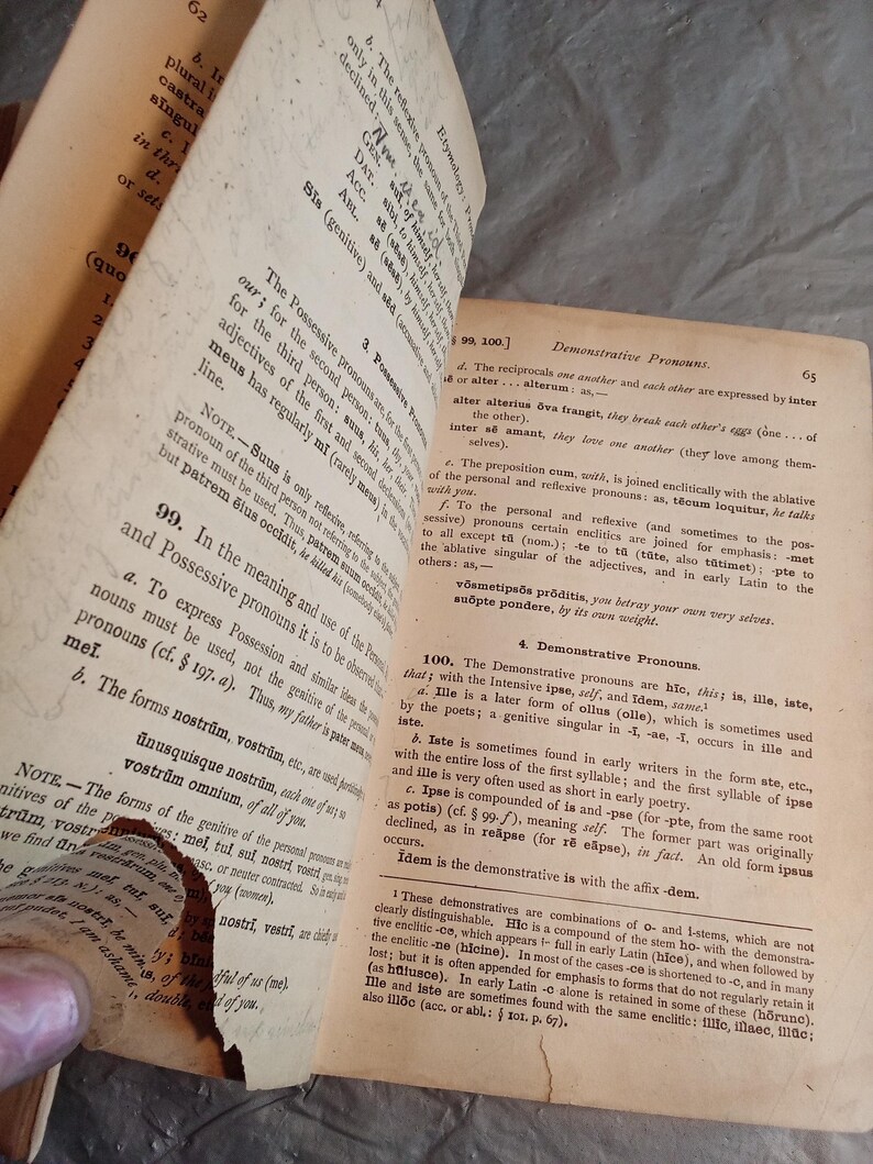 May include: Open book pages with text in Latin. The pages are aged and worn, with visible creases and a torn edge. The text is in black ink on yellowed paper, with headings and numbered sections.