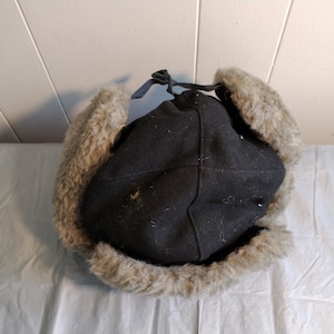 May include: A black wool trapper hat with a faux fur trim. The hat has a drawstring closure at the top.