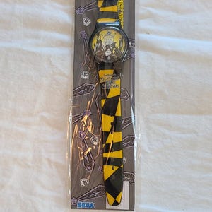 May include: Unopened wristwatch with a black and yellow striped strap. The watch face features characters from "The Nightmare Before Christmas." The watch is in its original packaging, with the SEGA logo visible.