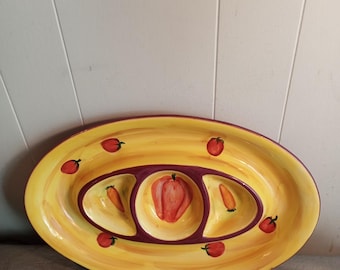 Puede incluir: Plato ovalado para servir con fondo amarillo y borde morado. El plato presenta tres secciones interiores, con un pimiento rojo grande en el centro y diseños de zanahorias y pimientos más pequeños. Ilustraciones de pimientos rojos están dispersas por el borde.