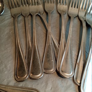 May include: A collection of silver forks with tines and teardrop-shaped handles. The forks are arranged in a close-up shot, showcasing their polished surfaces and classic design. The silverware is likely for a formal dining setting.