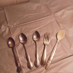 Puede incluir: Cinco piezas de cubiertos, incluyendo un tenedor, una cuchara y tres cucharaditas, están dispuestas sobre una superficie de color marrón claro. Los cubiertos están hechos de plata y tienen un acabado pulido.