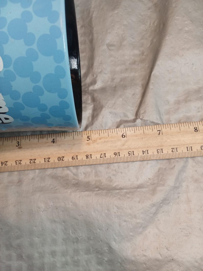 Pu&ograve; includere: Un bicchiere blu con bordo nero e sfondo azzurro con forme di testa di Topolino bianche. Il bicchiere &egrave; accanto a un righello di legno. Il bicchiere ha un diametro di circa 10 cm.