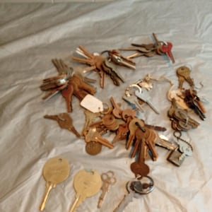 May include: A collection of various keys, including brass, silver, and rusty metal keys. Some keys are grouped together on rings, while others are loose. The keys are of different sizes and shapes, with some having decorative elements.